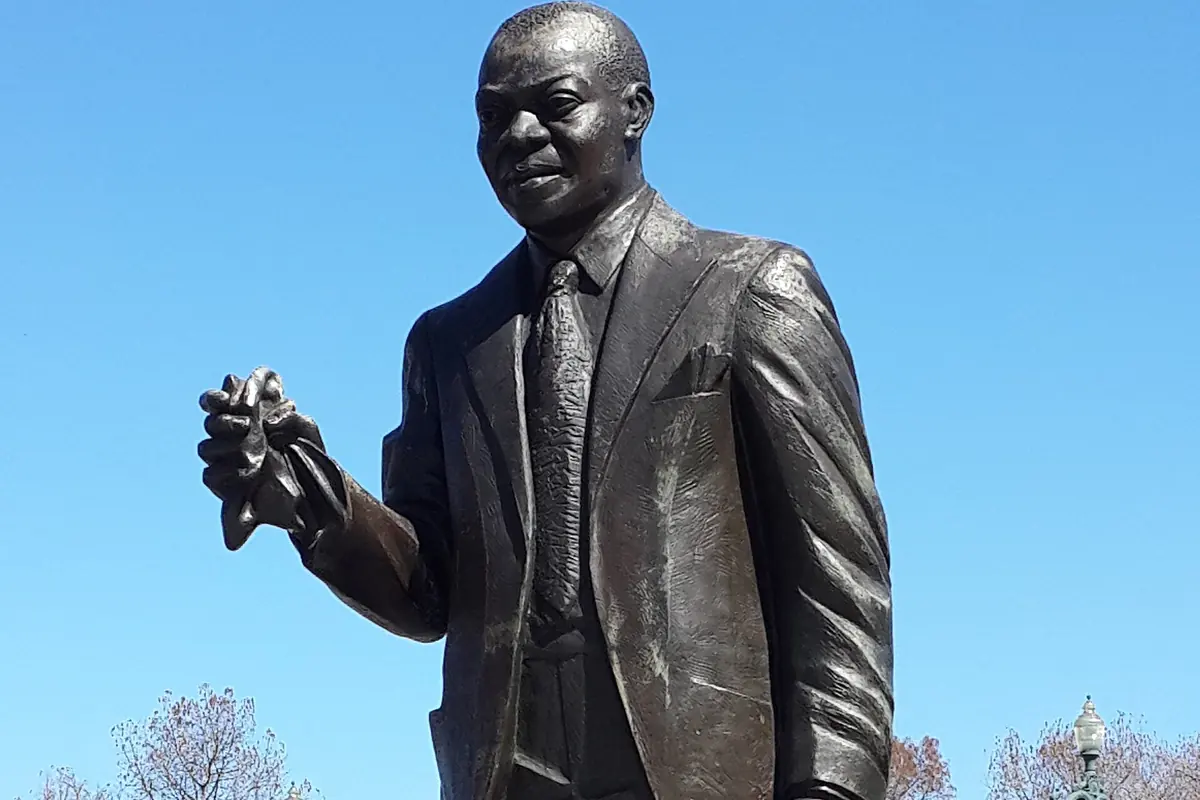 The bronze statue of Louis Armstrong in New Orleans, a smiling figure in a suit against a blue sky